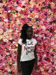 Young lady posing in front of a wall of flowers after her hair and makeup service