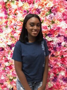 Young lady posing in front of a wall of flowers after her hair and makeup service