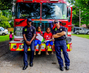 Two children and two fire fighters posing in front of a fire truck