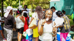 A group outside at an event on a sunny day, one girl facing the camera is smiling and eating cotton candy.