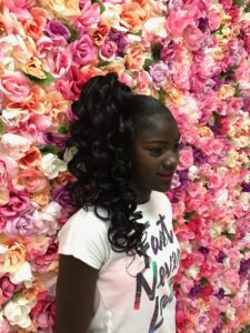 Young lady posing in front of a wall of flowers after her hair and makeup service