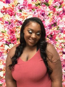 Young lady posing in front of a wall of flowers after her hair and makeup service