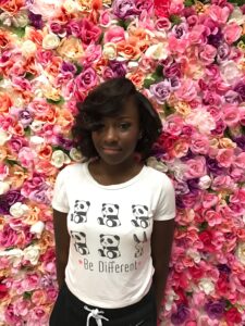 Young lady posing in front of a wall of flowers after her hair and makeup service