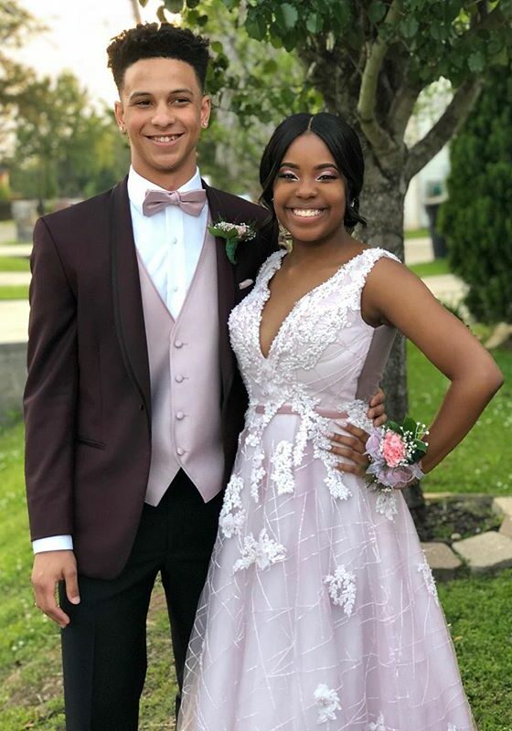 Two teenagers standing outside in a yard, smiling at the camera and dressed up for prom.